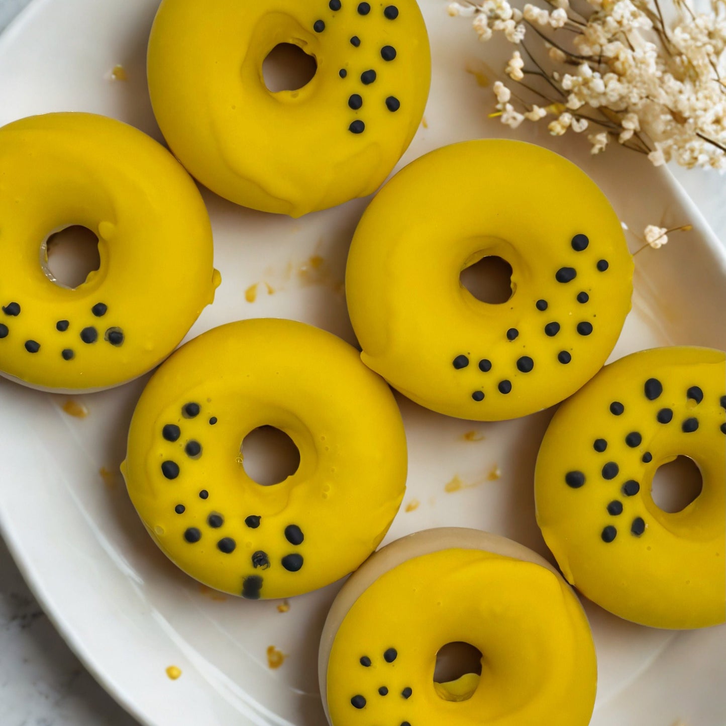 Yellow donut-shaped pastries with black specks on a white plate with dried flowers.
