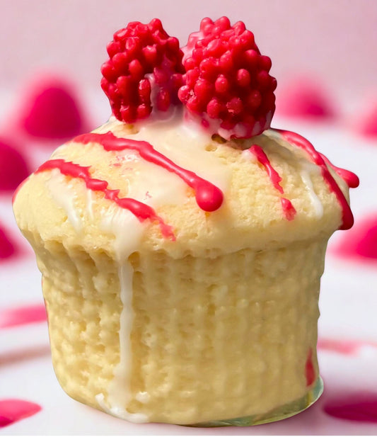Muffin with white icing and red drizzle, topped with raspberries on a pink background.